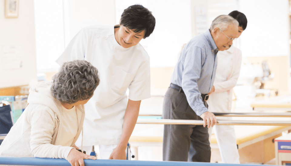 介護職員が高齢者の機能訓練をサポートしている様子。平行棒を使った歩行訓練。